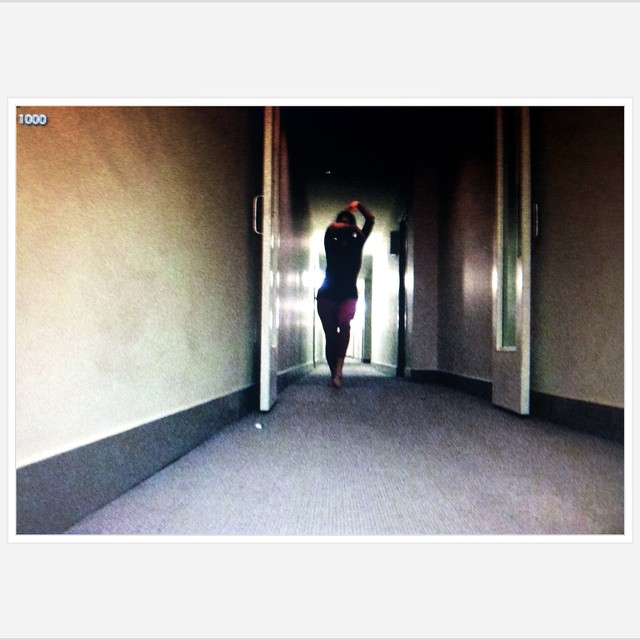 A dancer performs in a dark hallway. Her arms mask her face. 